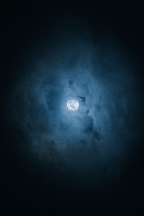 Free A captivating view of a full moon surrounded by clouds, creating an ethereal night scene. Stock Photo