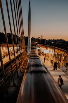 A high-speed train arriving at a busy urban station at dusk with commuters.