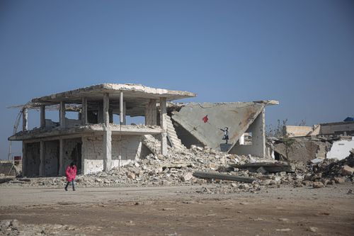 Free A child in a pink coat walks near a war-torn building with an artwork on the wall. Stock Photo
