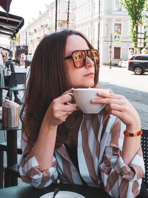 Free Stylish woman with sunglasses enjoys a coffee at an outdoor cafe in the city. Stock Photo