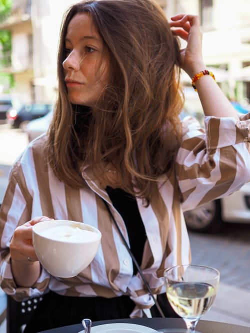 Free A young woman with a ceramic cup in hand sits at an outdoor cafe, enjoying her drink. Stock Photo