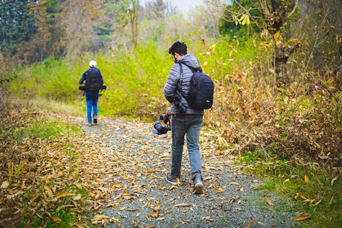 A Man Carrying a Camera Walking on the Unpaved Foot Path in the Forest