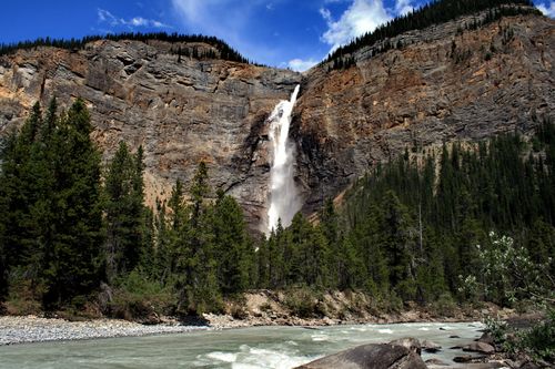 Free A stunning waterfall cascading down a rocky cliff surrounded by lush forest and river. Stock Photo