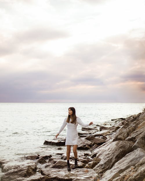 A Woman Walking on the Rocky Shore Near the Sea