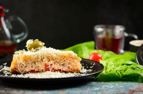 Free A delicious slice of focaccia topped with cheese and olives on a black plate, garnished with fresh greens. Stock Photo