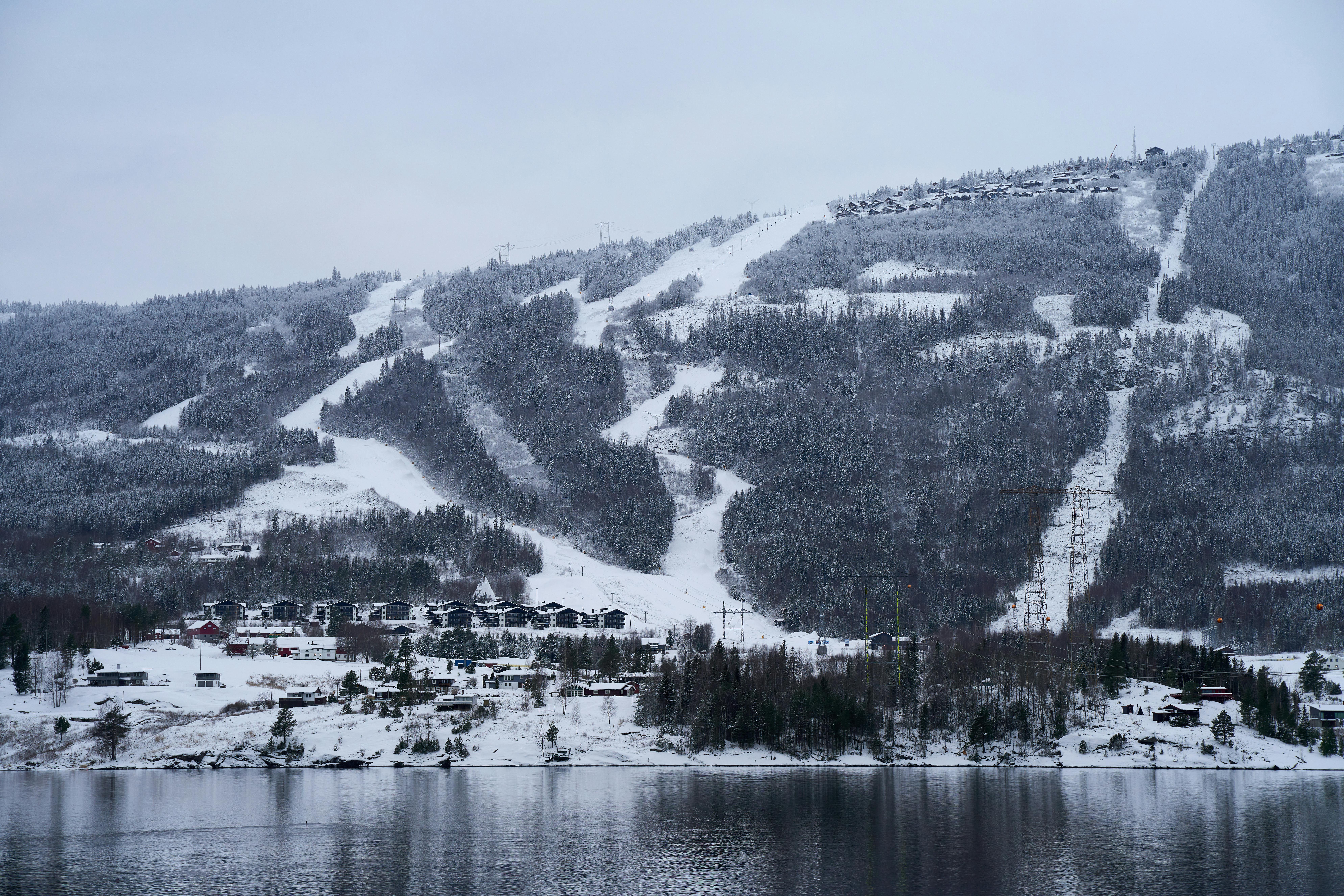 Scenic snowy mountain landscape with ski slopes and lake, showcasing Norway's winter beauty.