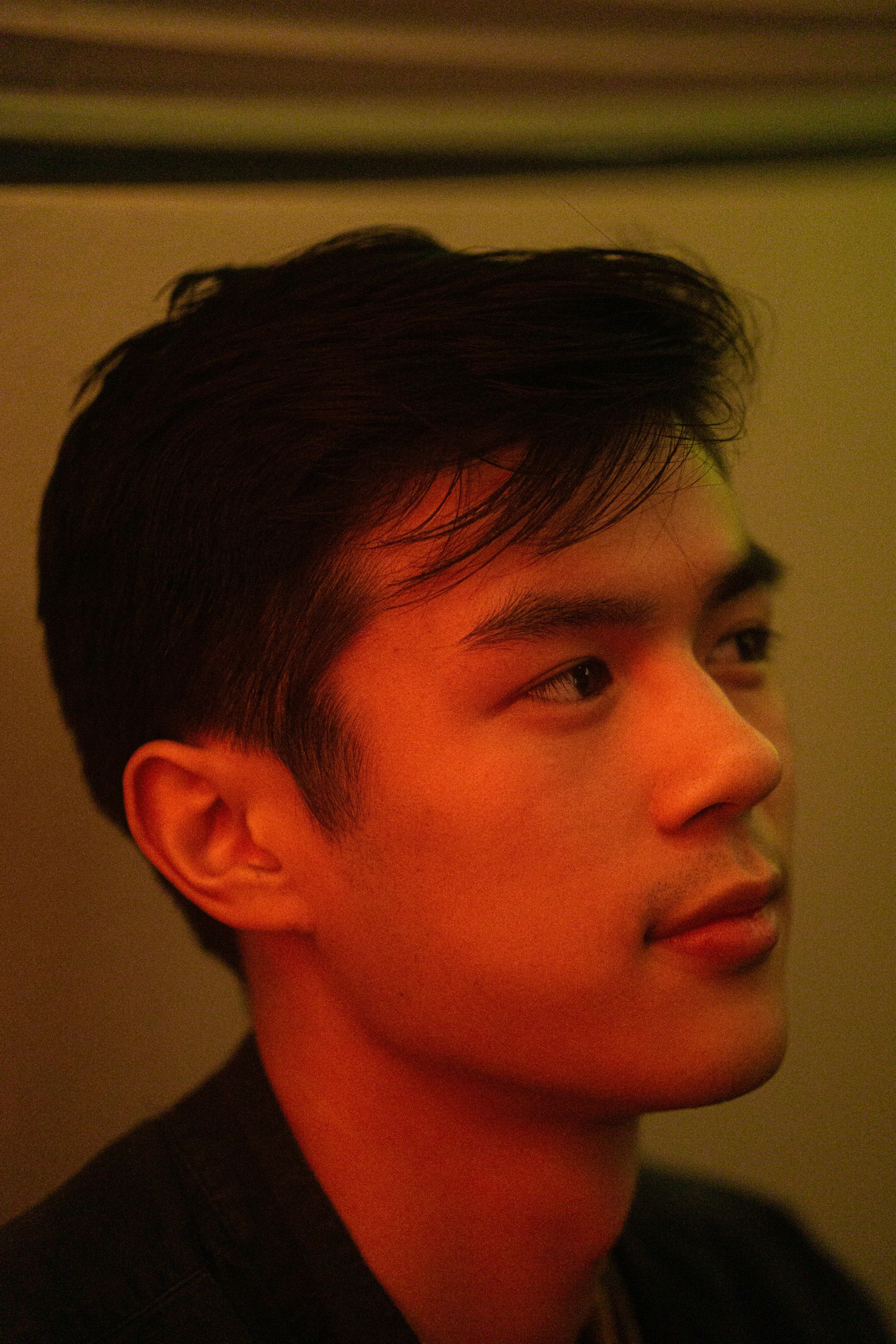 A side view portrait of a young man with warm and moody lighting, conveying a contemplative mood.