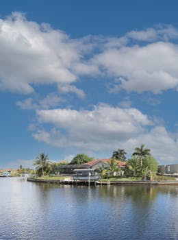 Scenic view of a tropical waterfront home in Cape Coral, Florida with palm trees and blue sky.