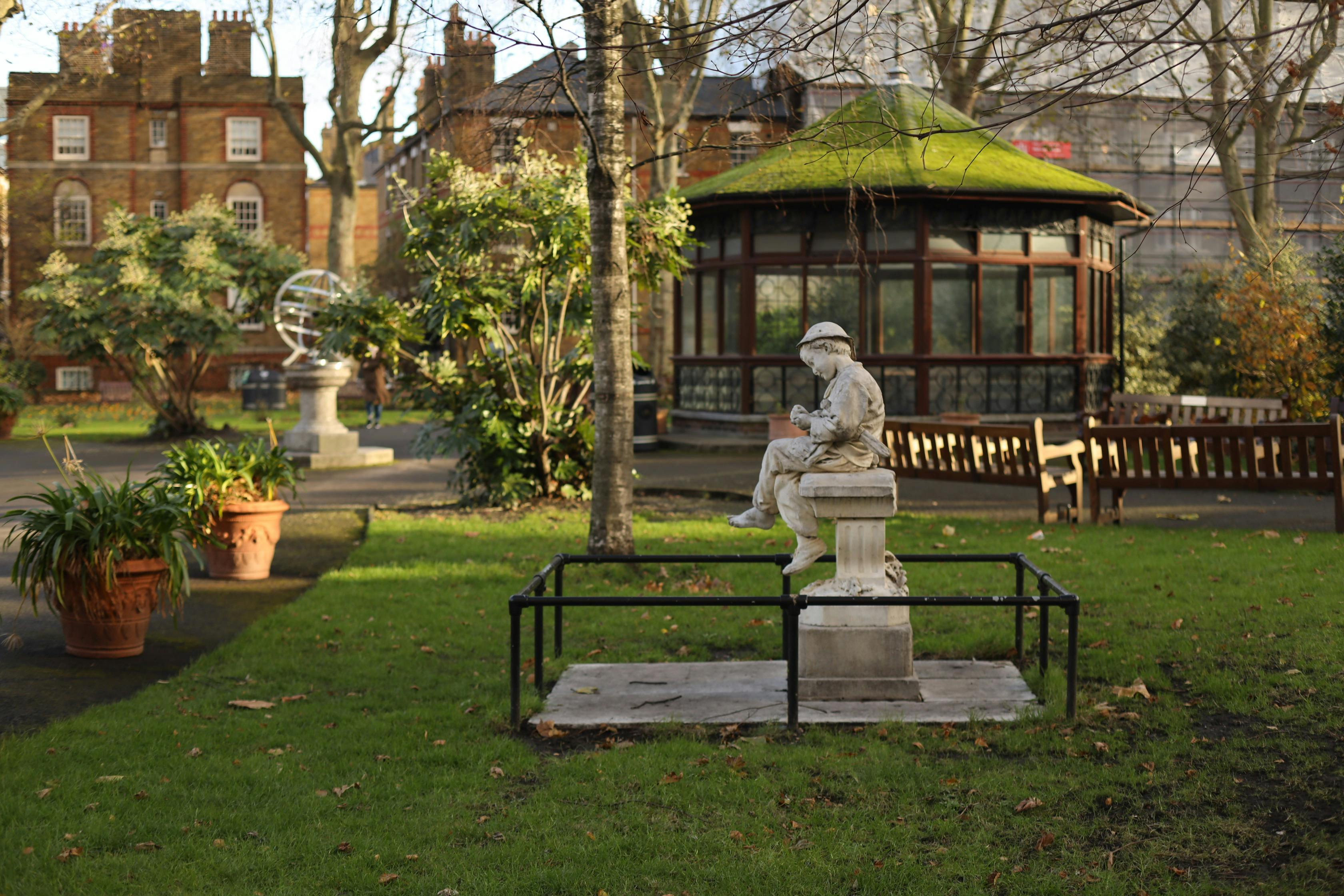 A picturesque park scene featuring a statue, pavilion, and lush greenery on a sunny day