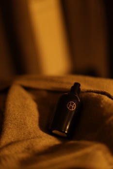 Black bottle positioned on a warm, textured fabric surface with a blurred background effect.