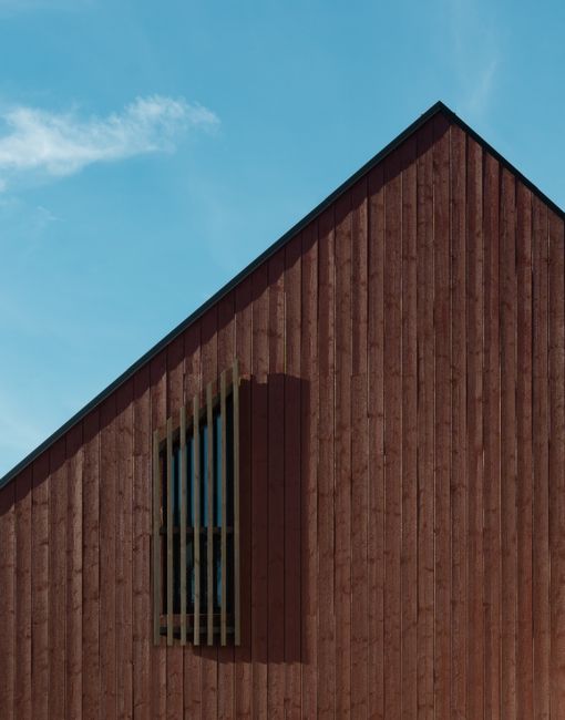A geometric minimalist wooden facade with a window against a clear blue sky in Son, Norway.