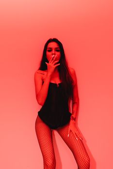 A woman in lingerie poses against a red backdrop, exuding sensuality and confidence.
