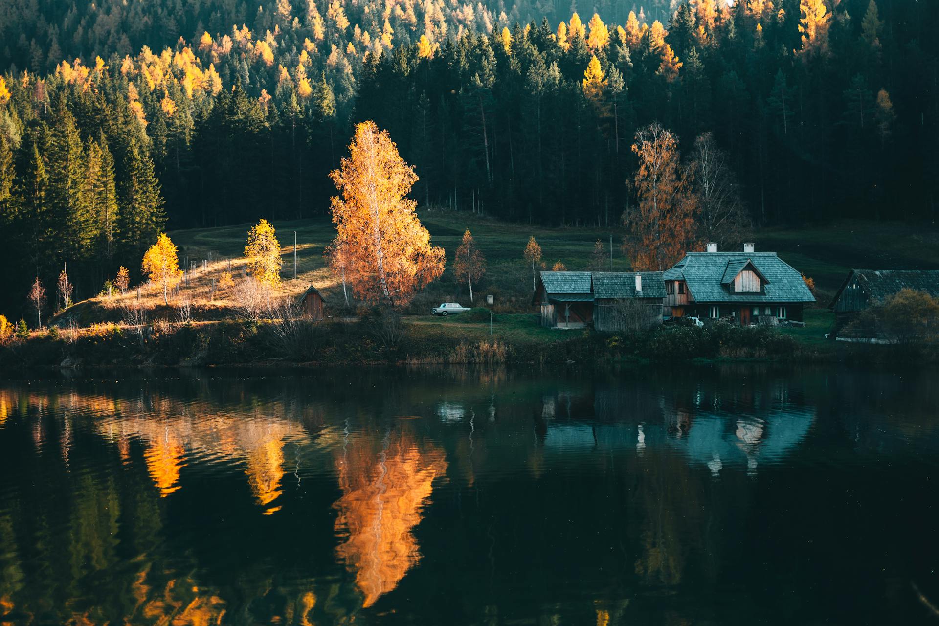 Idyllic autumn forest scene with lodge and perfect water reflection at lakeside.