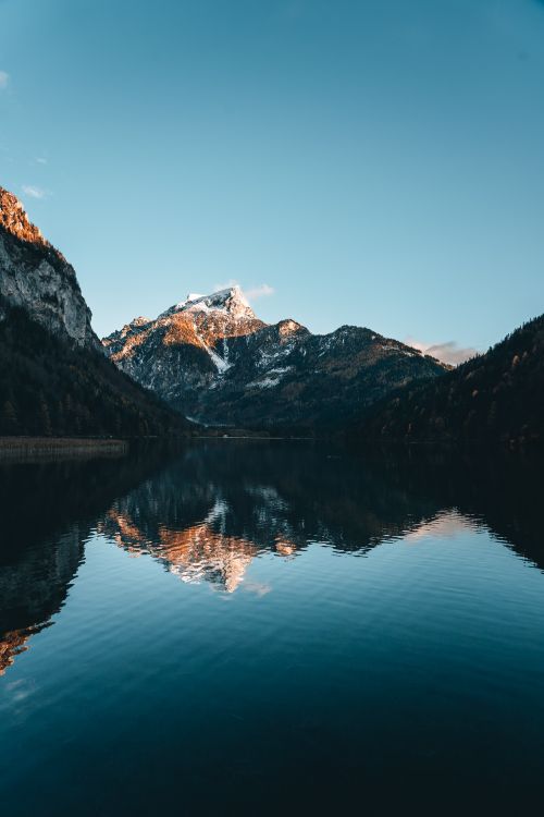 Free Snow-capped mountains reflecting on a serene lake under clear skies, creating tranquil landscape scenery. Stock Photo