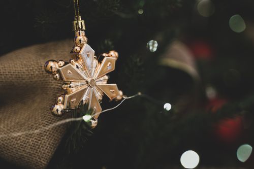 Free Close-up of a gold snowflake ornament hanging on a decorated Christmas tree with bokeh lights. Stock Photo