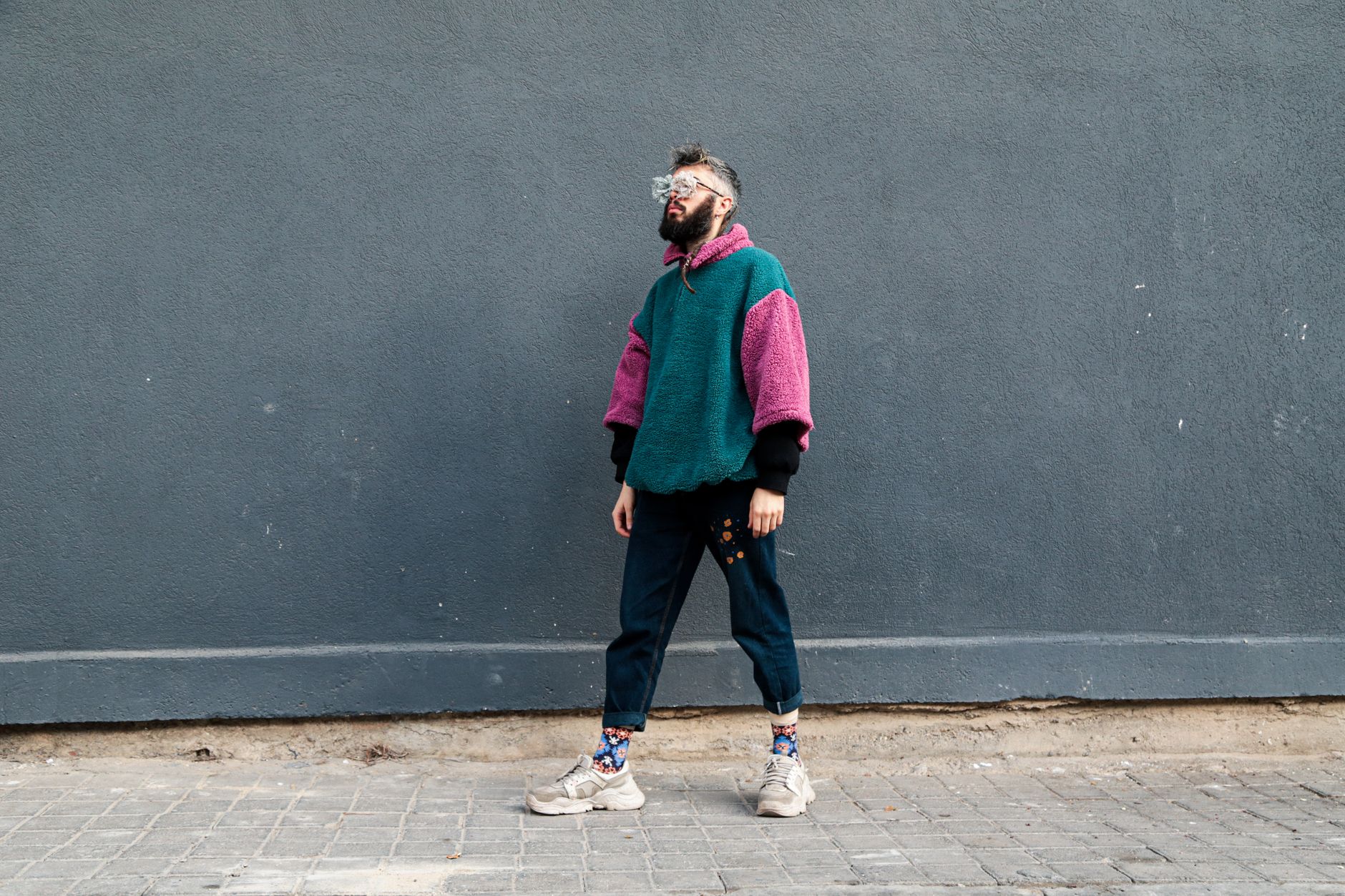 Homme stylé en pull streetwear coloré posant devant un mur gris en ville