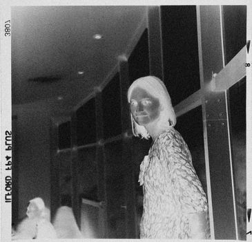 A black and white film negative showcasing a woman standing indoors with a vintage feel.