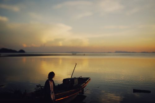 Free Idyllic scene of a person and boat at sunset by a peaceful lake shore. Stock Photo