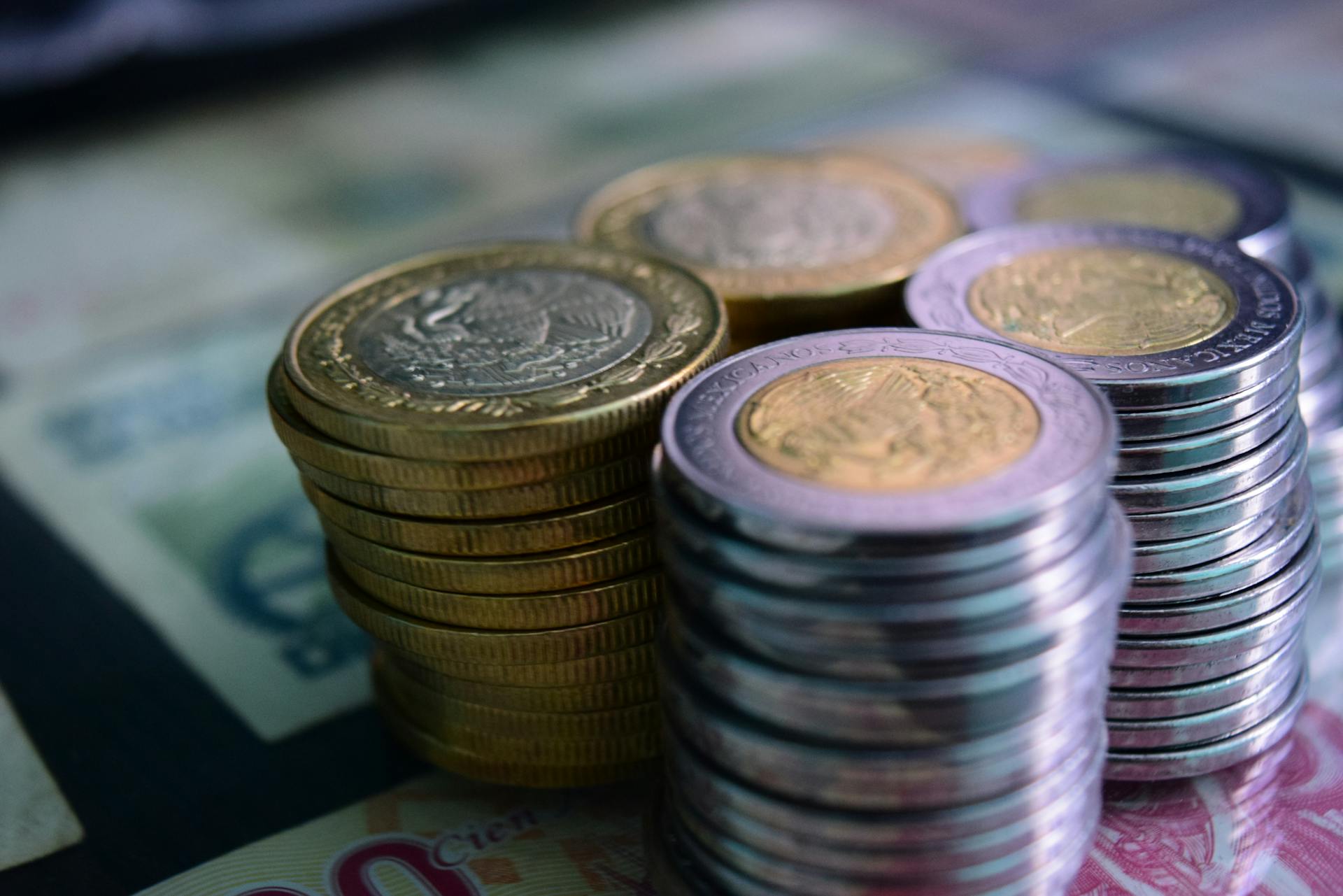 Close-up of stacked gold and silver coins on various currency notes, symbolizing wealth and savings.