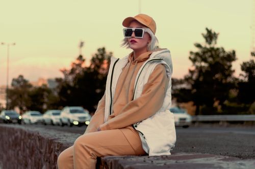 Free Stylish woman in beige outfit and sunglasses sitting on a wall in Tehran at sunset. Stock Photo