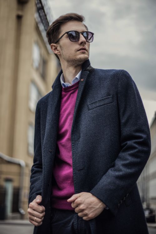 Free Stylish man in pink sweater and gray coat posing outdoors in urban setting. Stock Photo