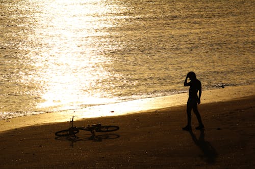 Silhouette of Man Standing on the Beach Near the Bicycle