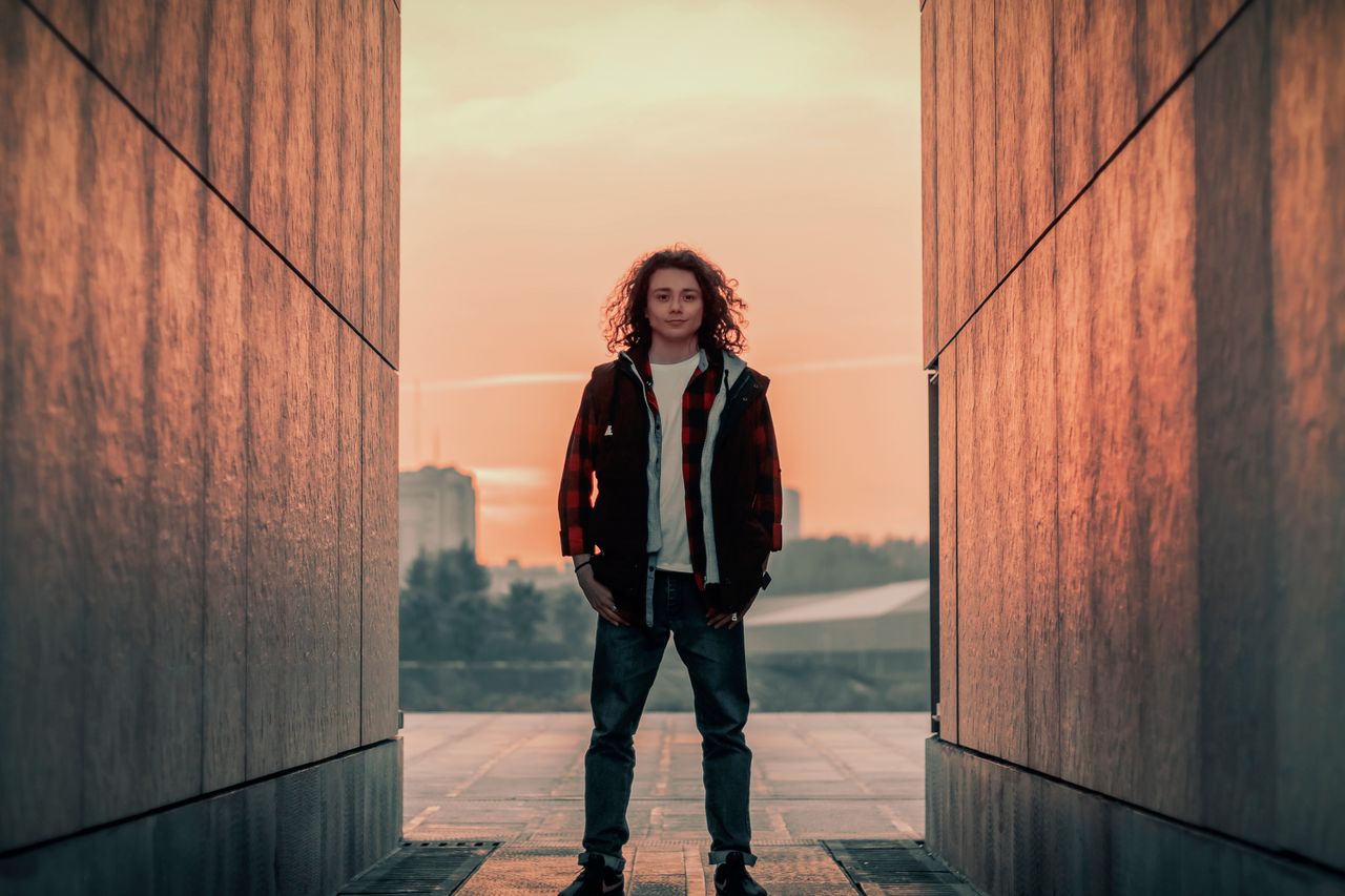 man with curly hair in plaid jacket standing confidently between city