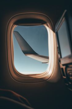 A scenic view of an airplane wing through a window, flying high above the clouds.