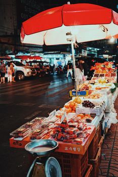 Colorful fruit stall under a red umbrella at a lively nighttime market.