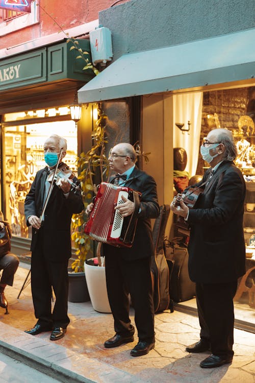Men in Black Suit Playing Music on the Side of the Street Near Business Establishment
