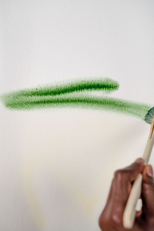 Free A detailed view of a hand painting a green stroke on a canvas with a paintbrush. Stock Photo