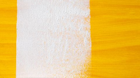 A close-up of a paint roller creating a white stripe on a vibrant yellow surface.