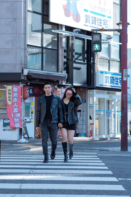 Free A stylish couple walks across a city street, embracing a modern urban feel. Stock Photo