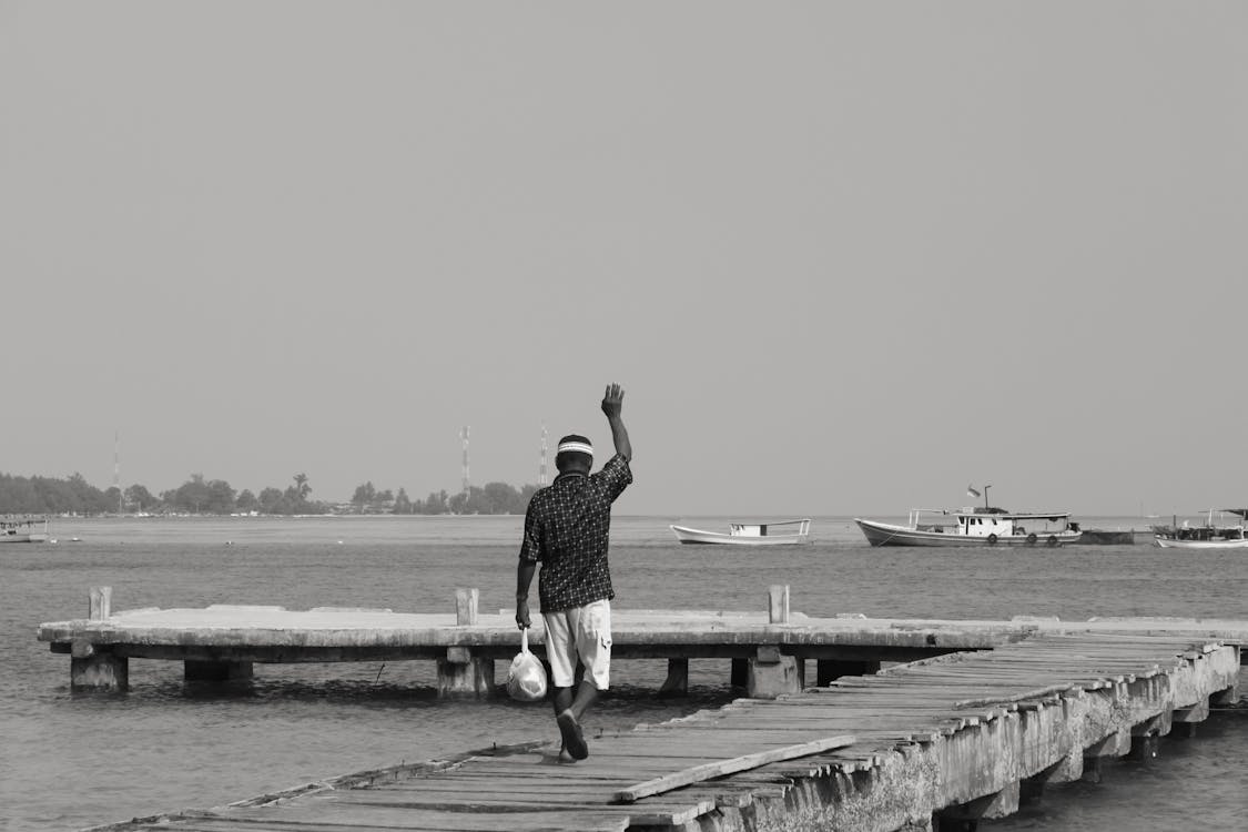 Free Grayscale Photo of a Man Walking on Wooden Dock Waving Stock Photo