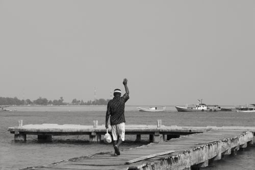 Free A man walks on a dock in Jakarta, waving goodbye on a grayscale day by the sea. Stock Photo