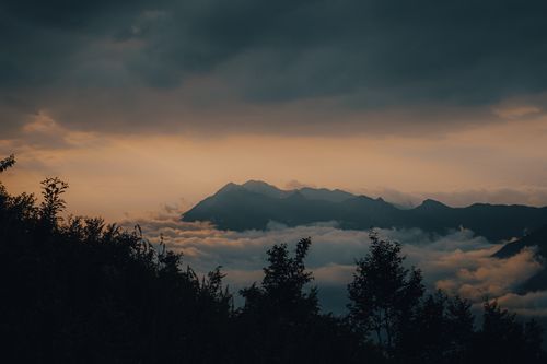 Free Scenic view of a mountain silhouette surrounded by clouds at sunset, perfect for nature lovers. Stock Photo