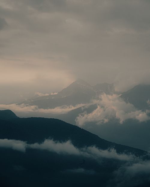 Free A serene mountain landscape enveloped in fog and gray clouds, ideal for nature-themed visuals. Stock Photo