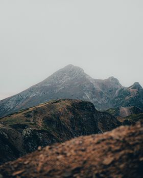 Misty view of rugged mountain peaks under a white sky, showcasing natural beauty.