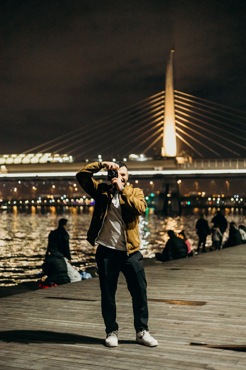 Man photographing the vibrant night scene by the Golden Horn Metro Bridge in Istanbul, Turkey.