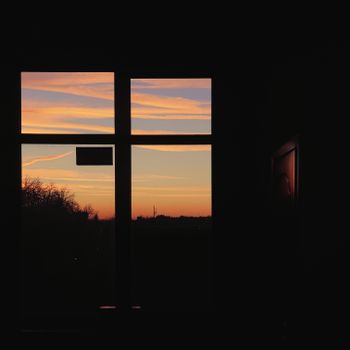 A tranquil sunset with colorful skies visible through a silhouetted window frame.