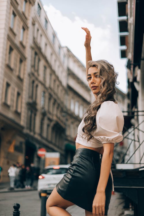 Woman in White Blouse and Leather Skirt Standing on Street Side