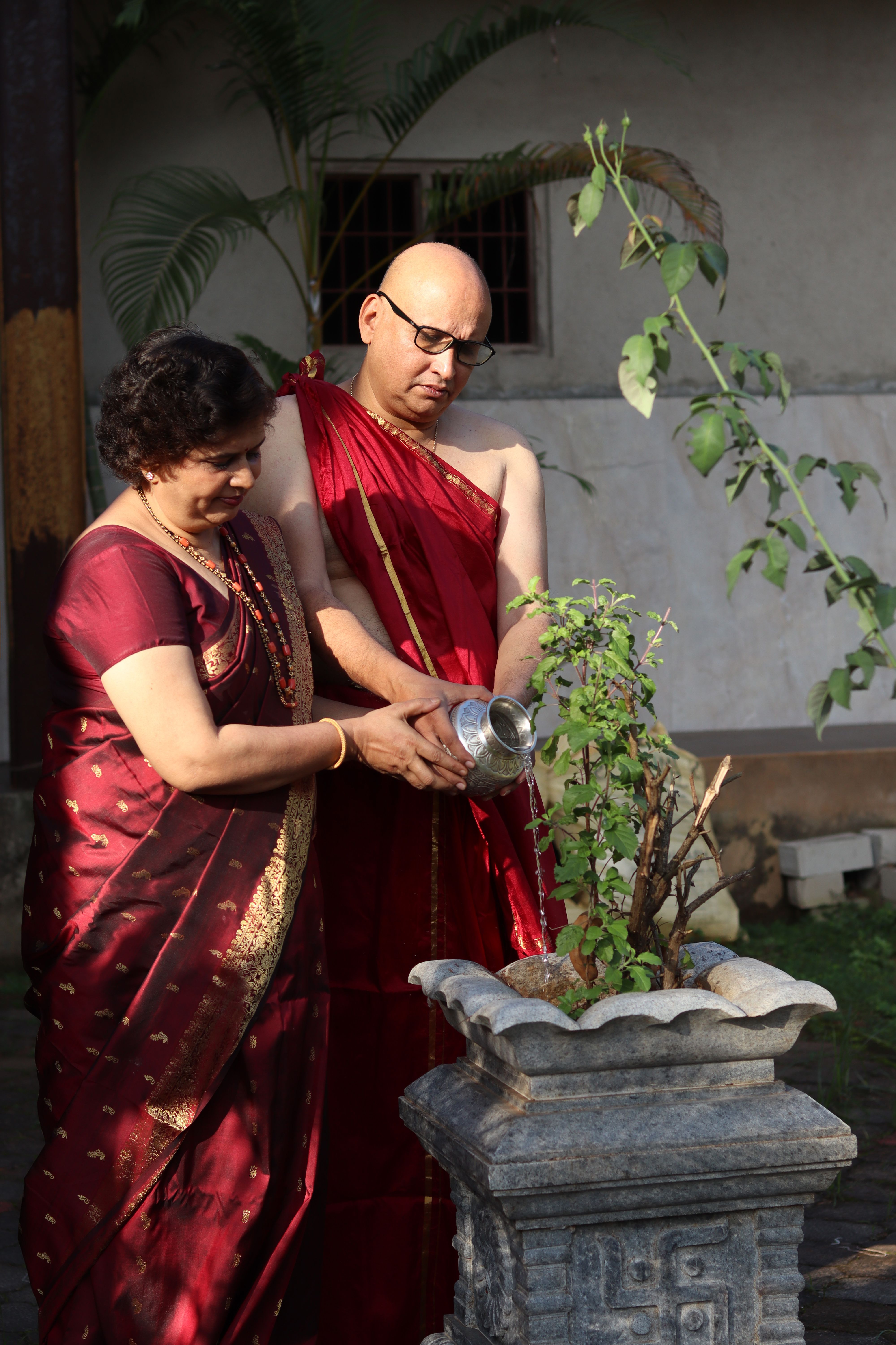 An elderly couple dressed in traditional attire caring for a plant outdoors.