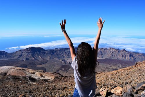 Free A woman celebrates atop Mount Teide with arms raised, overlooking the vast landscape and sea. Stock Photo