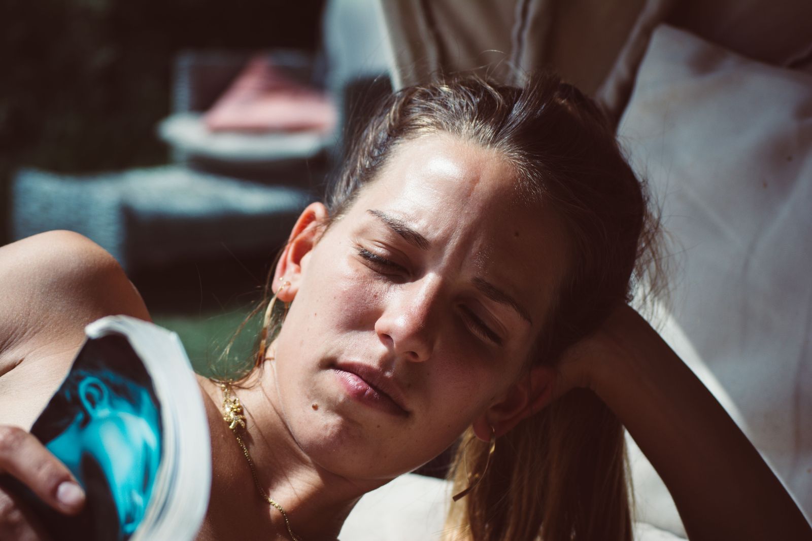 Woman with pulled-back hair reads a magazine in warm sunlight, resting her head on her hand