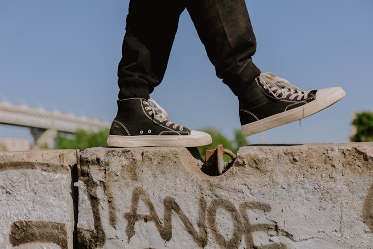 A Person Wearing Black Sneakers Walking On Concrete Wall