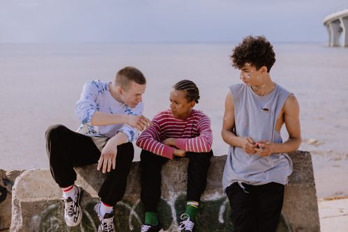 Free Teenagers sitting on a graffiti-covered wall by the sea, enjoying the day together. Stock Photo