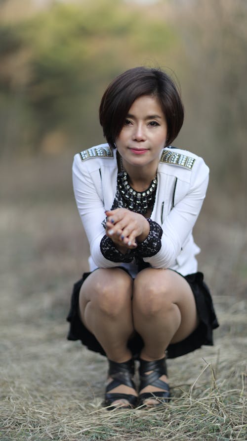 Woman in White Long Sleeve Shirt and Black Skirt Sitting on Green Grass