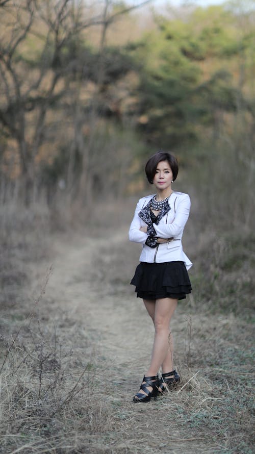 A Woman in White Long Sleeve and Black Skirt Standing on Pathway with Grass