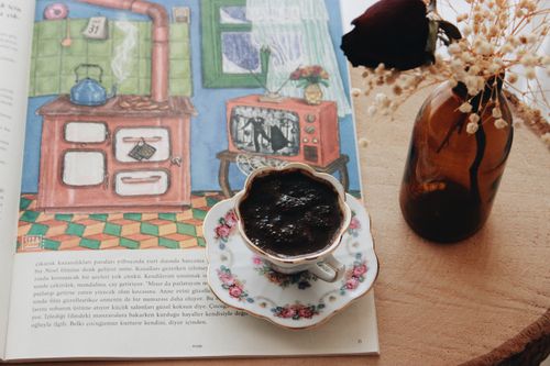 Free A cozy scene featuring Turkish coffee, floral decor, a book, and a rustic glass bottle on a wooden surface. Stock Photo