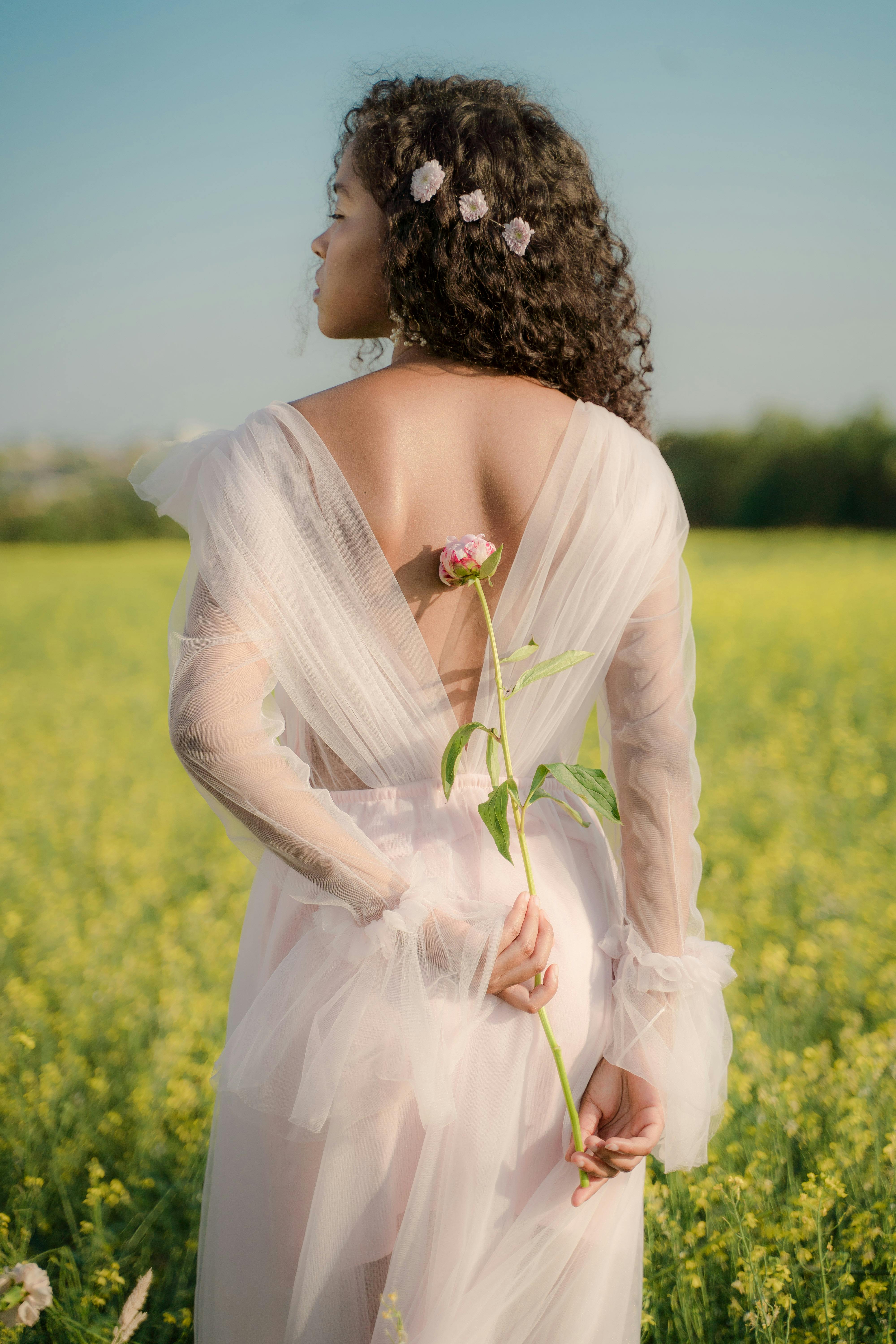 attractive woman in tulle white dress holding rose behind back